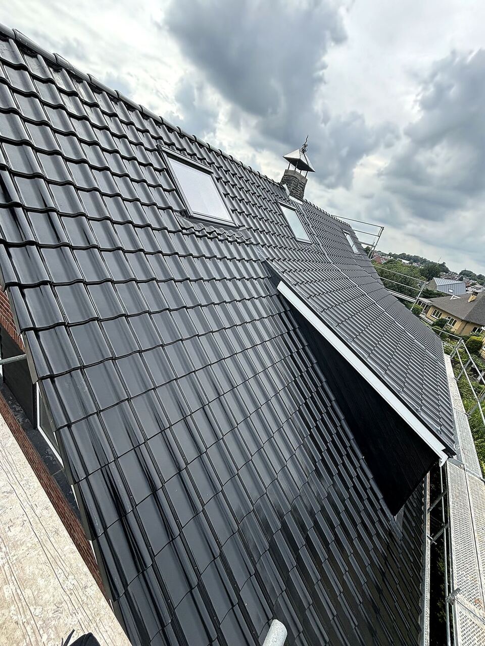 Toiture à Dilbeek après rénovation : tuiles anthracite, vue sur les velux et la cheminée